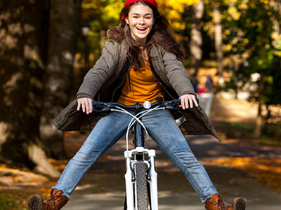 Ein glücklich lächelndes Mädchen fährt Fahrrad in einem Park, während es fröhlich die Beine ausstreckt.